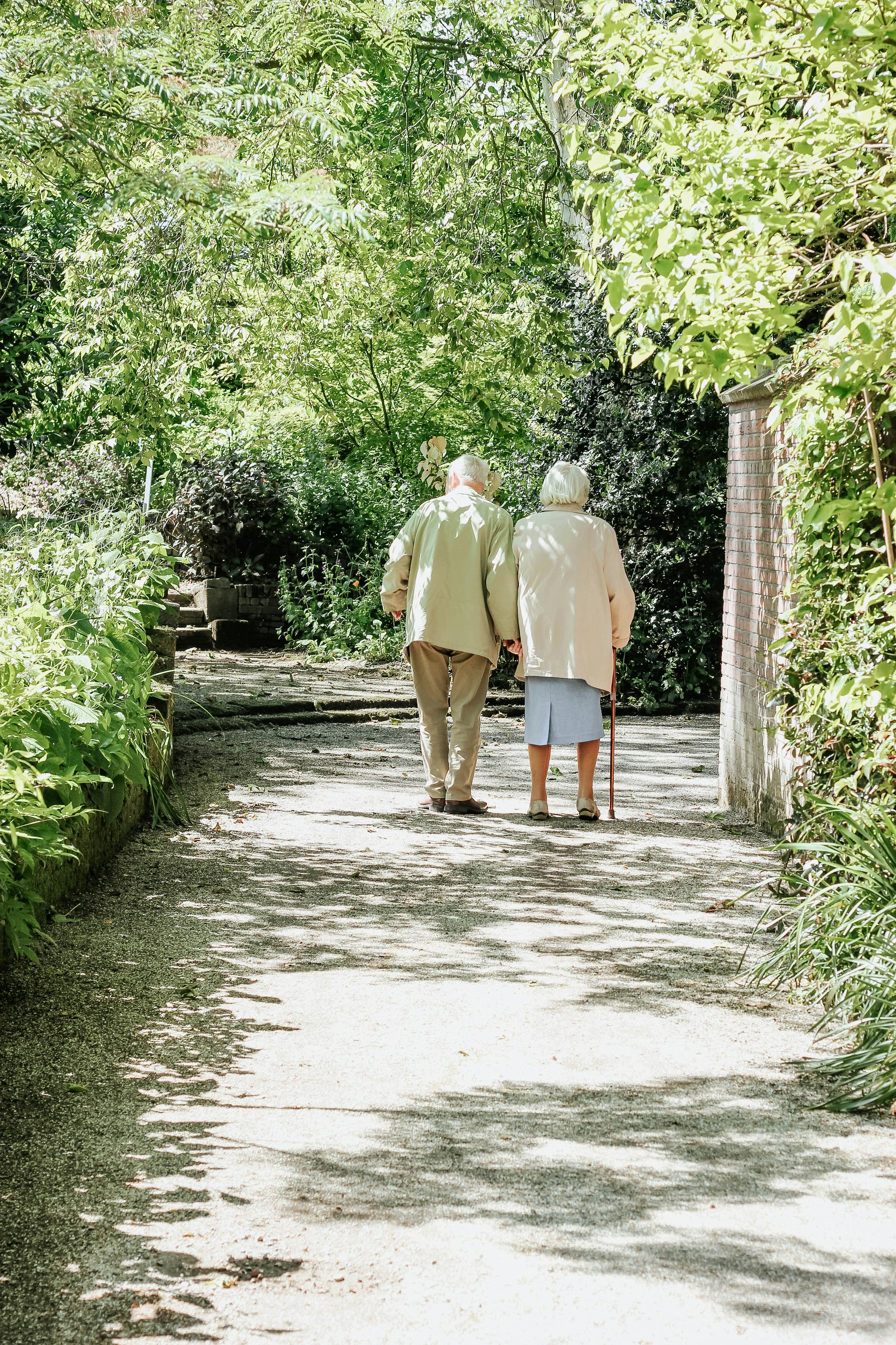 An older couple walking together along a tree-lined path