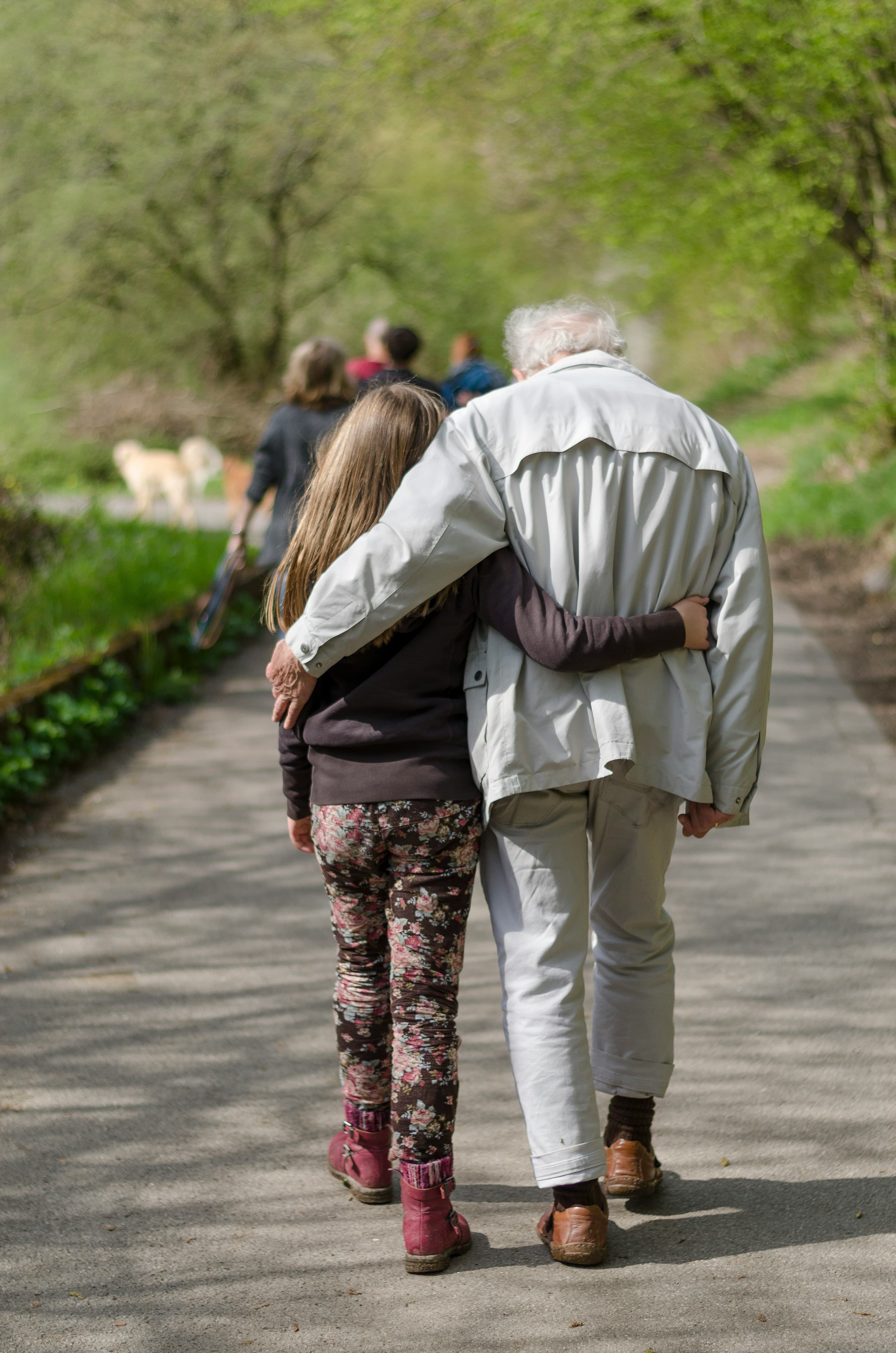 A grandparent and grandchild walking arm in arm along a quiet path